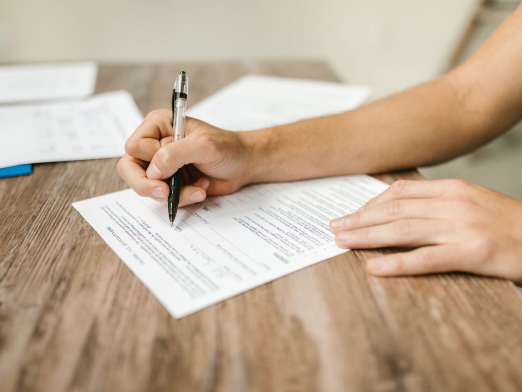 Hand filling out paperwork with a pen, showcasing focus on document completion