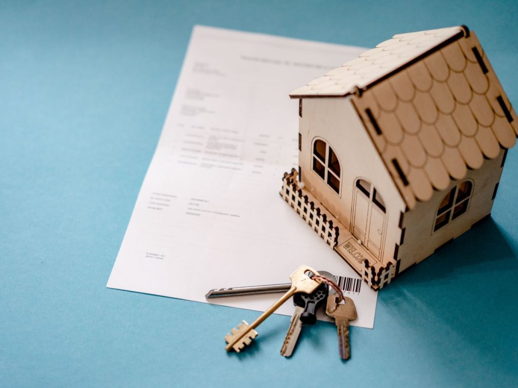 Miniature wooden house with keys and contract symbolizing real estate transactions