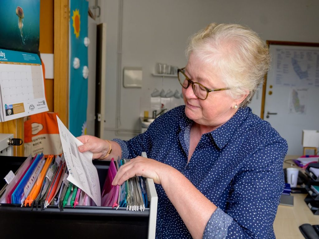 Elderly woman sorting paperwork in an office setting with organized files