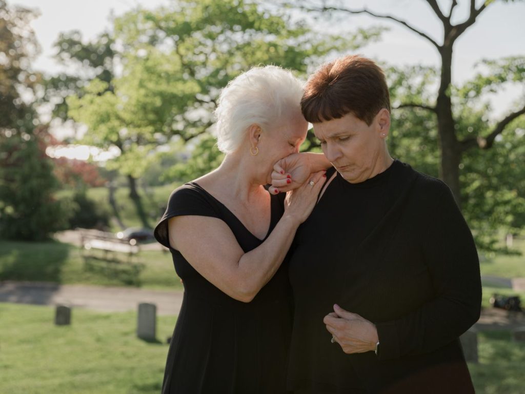 Two women embracing and grieving in an outdoor cemetery setting