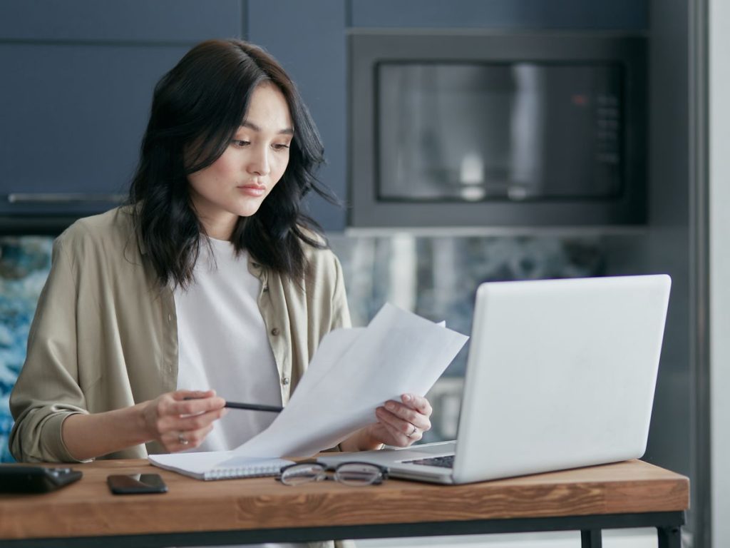 Woman reviewing documents and working on a laptop at a home office