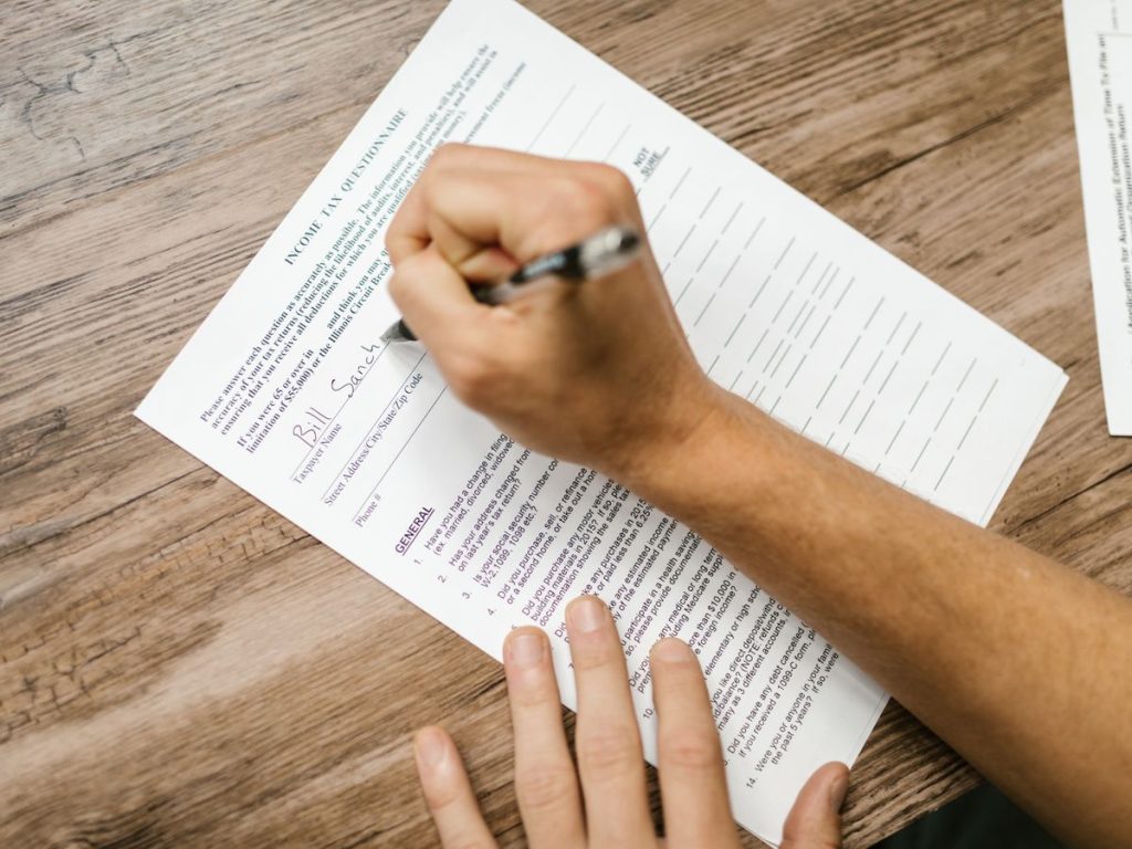 Person filling out a tax questionnaire with a pen, showing close-up on wooden table