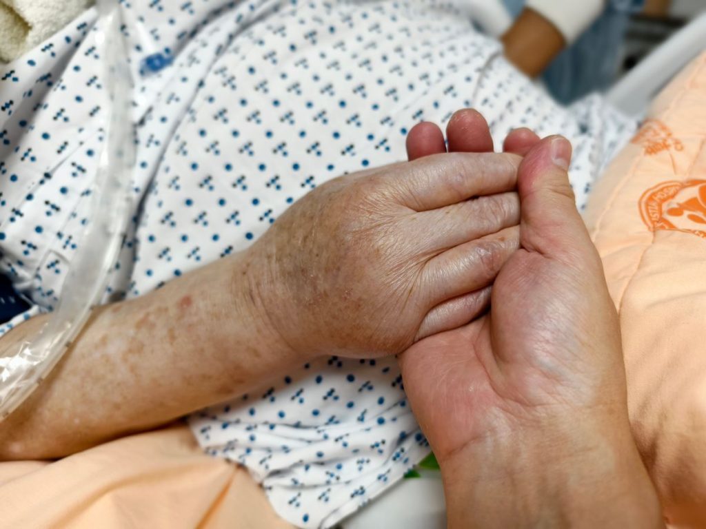 Close-up of hands holding in a hospital setting, symbolizing compassion and care