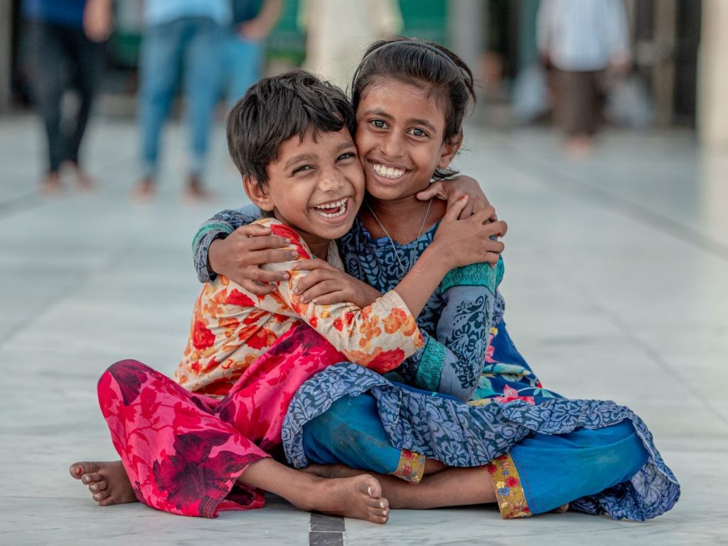 Two smiling children sit and hug outdoors, exuding warmth and joy