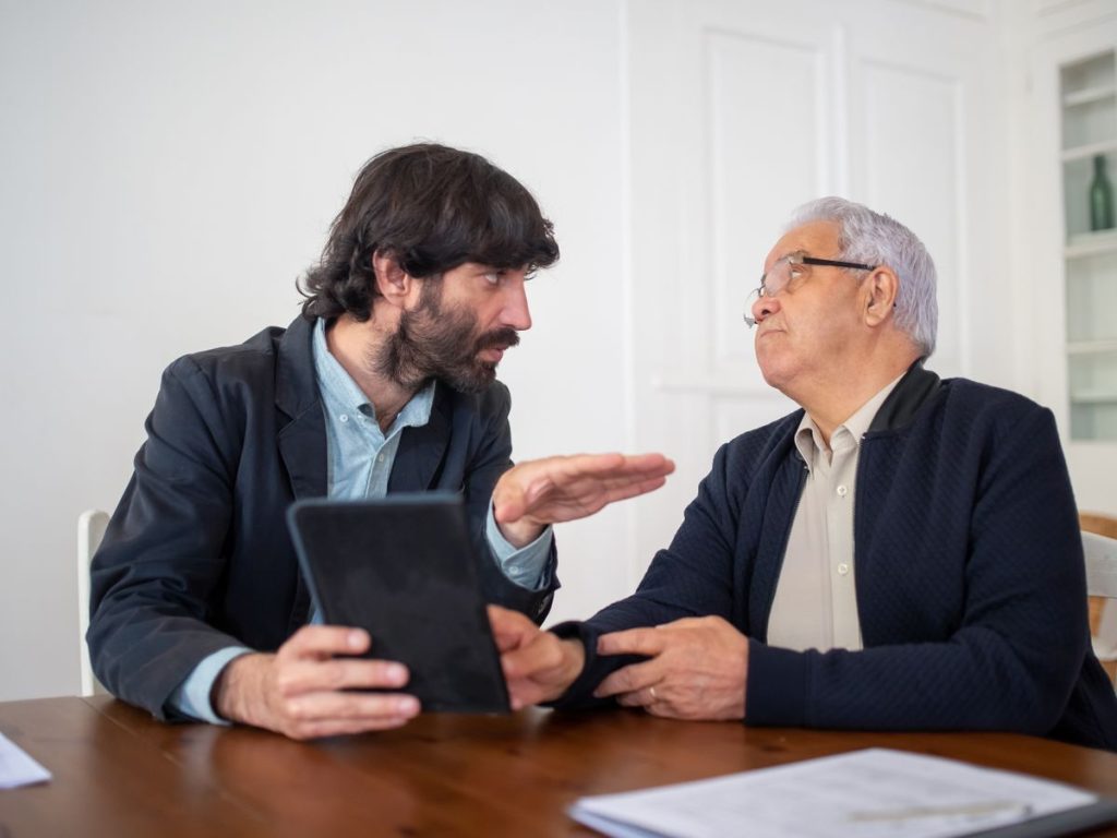 Adult son and his older father talking over a tablet at a table