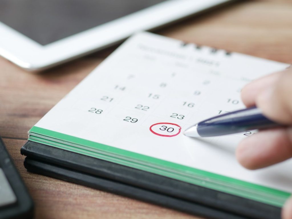 Close-up shot of a hand marking a date on a calendar with a pen, emphasizing planning and scheduling