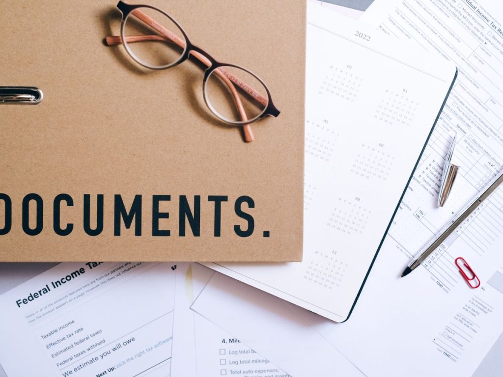 Flat lay of office supplies including documents, calendar, and eyeglasses on a desk
