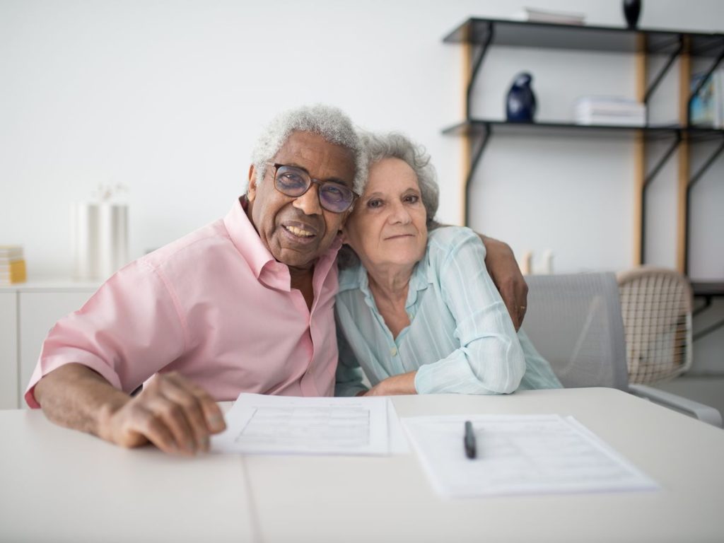 Elderly couple smiling and hugging while looking at documents on table indoors