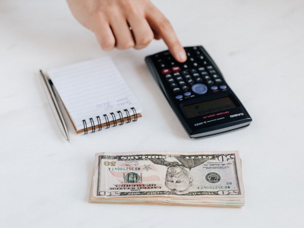 Person using a calculator while counting cash and reviewing bills