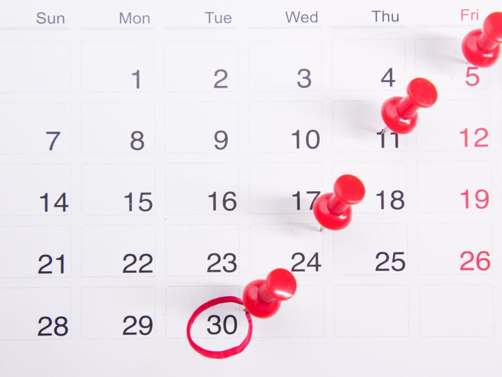 Close-up of a calendar with red push pins marking important dates, emphasizing deadlines