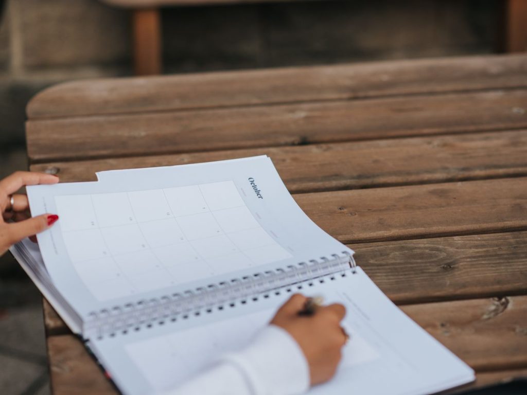 Crop anonymous female student writing in planner while sitting at wooden table in park