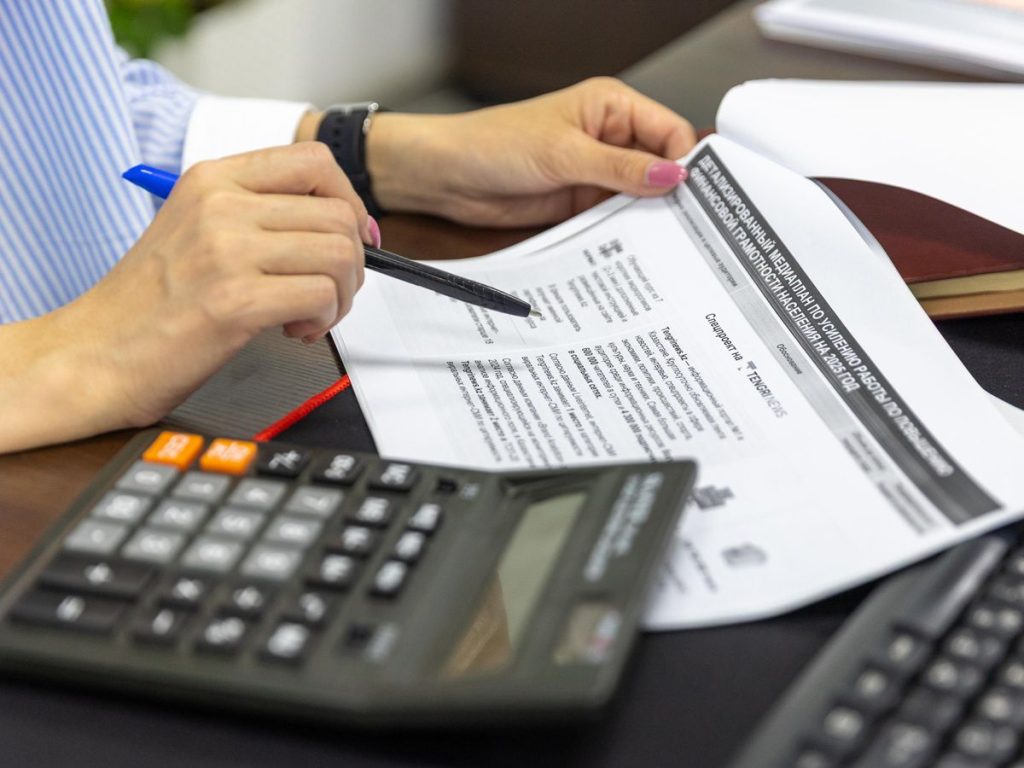 Close-up of a person analyzing financial documents using a calculator and pen