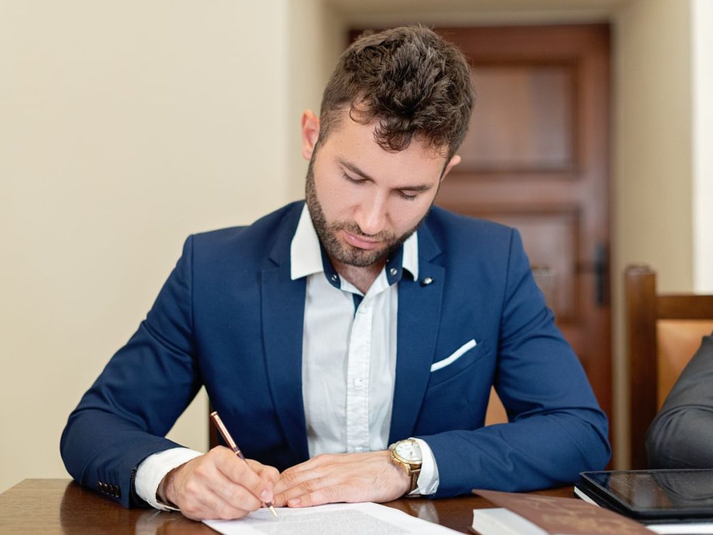 Confident businessman in a suit signing a contract at the office desk