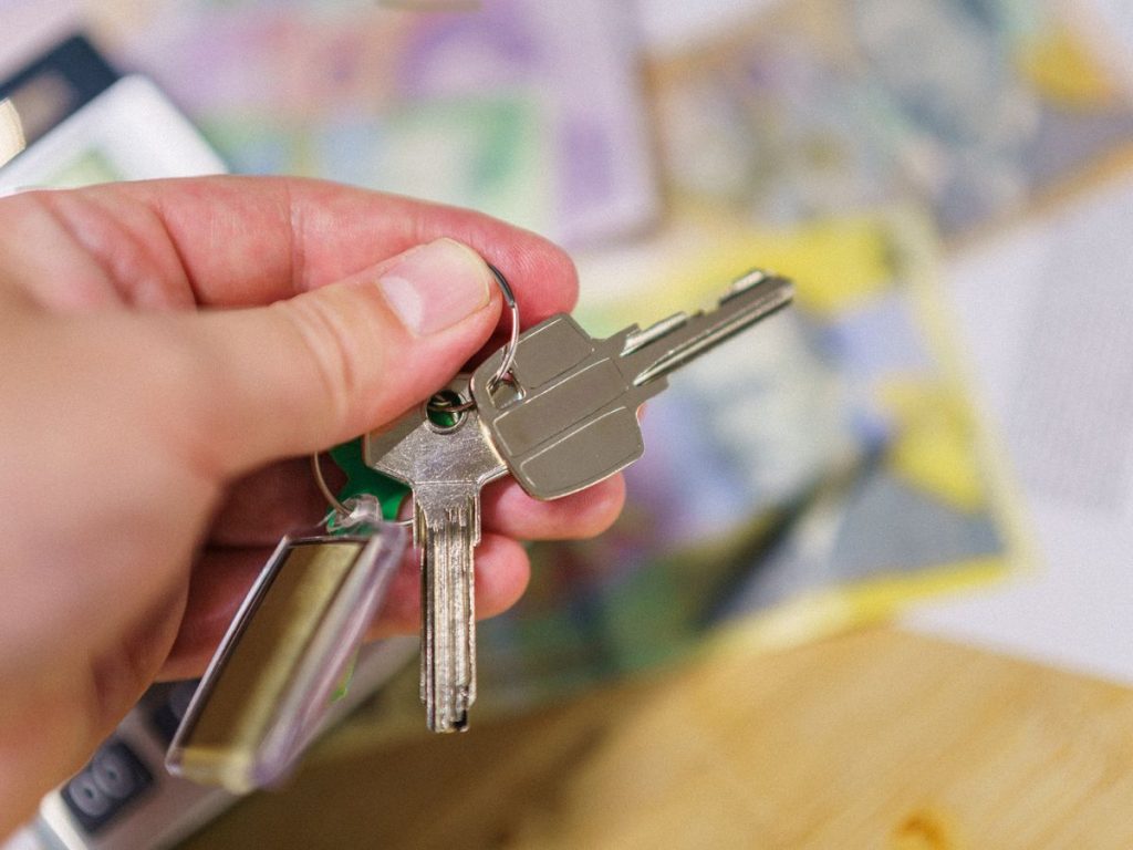 Close-up of keys in hand representing property ownership with blurred financial documents in the background