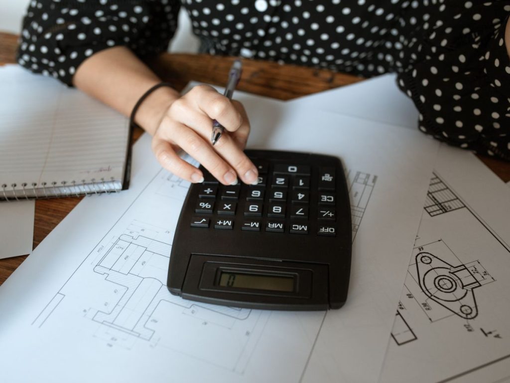 Close-up of an architect's hand using a calculator on technical drawings with a polka dot shirt
