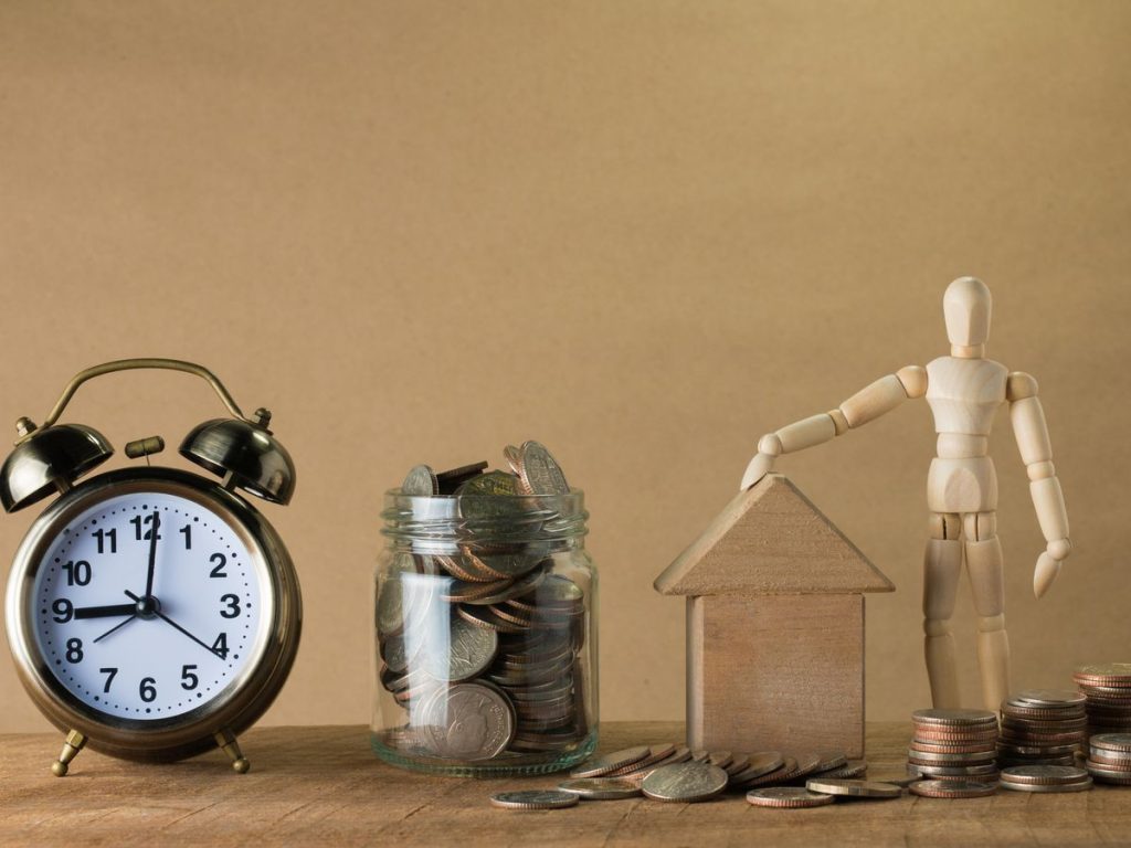 Wooden mannequin with a house, coins, and clock symbolizing time and financial planning