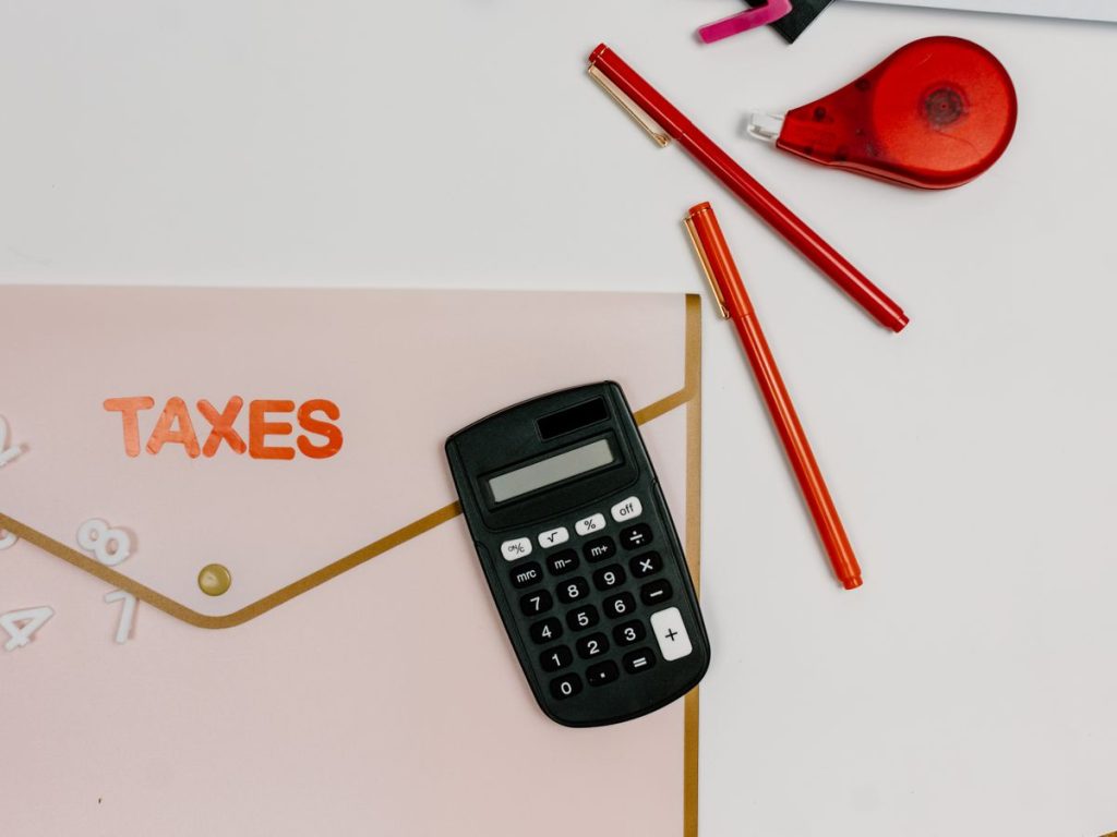 Flat lay image featuring a calculator, pens, and a folder labeled 'TAXES'