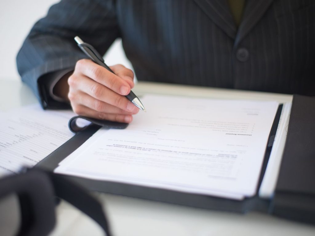 Close-up of a hand signing documents with a pen, symbolizing an important business contract