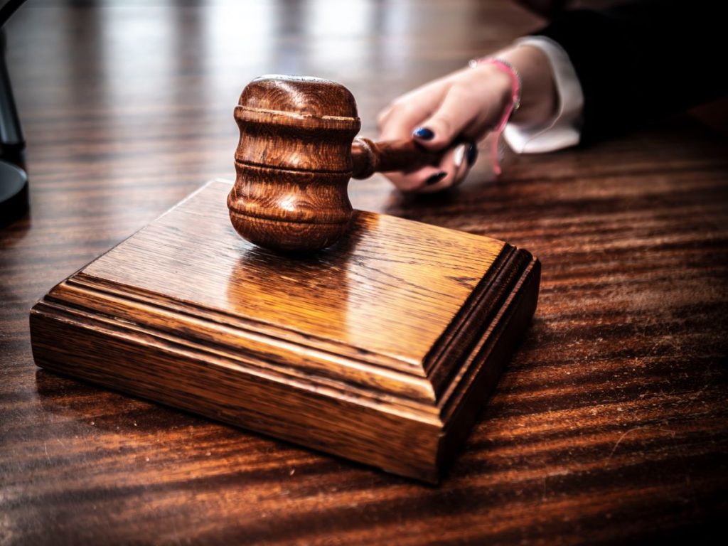 Close-up image of a wooden gavel held by hand on a desk in a courtroom setting