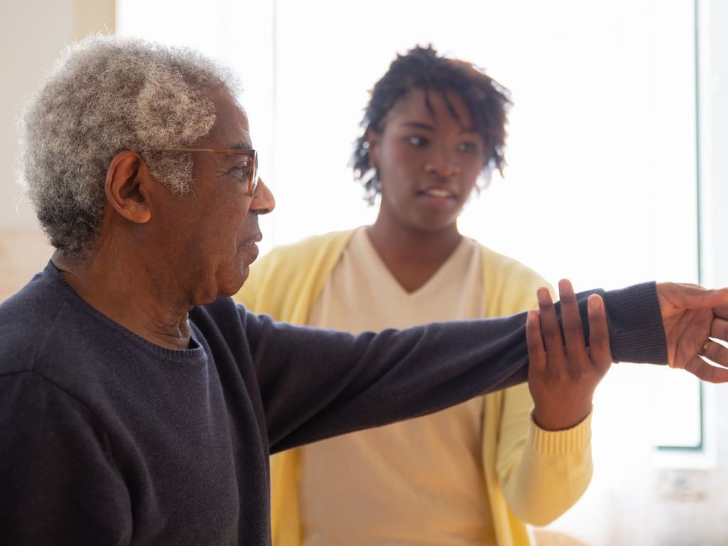 A caregiver helps an elderly man with arm exercises in a warm and caring environment