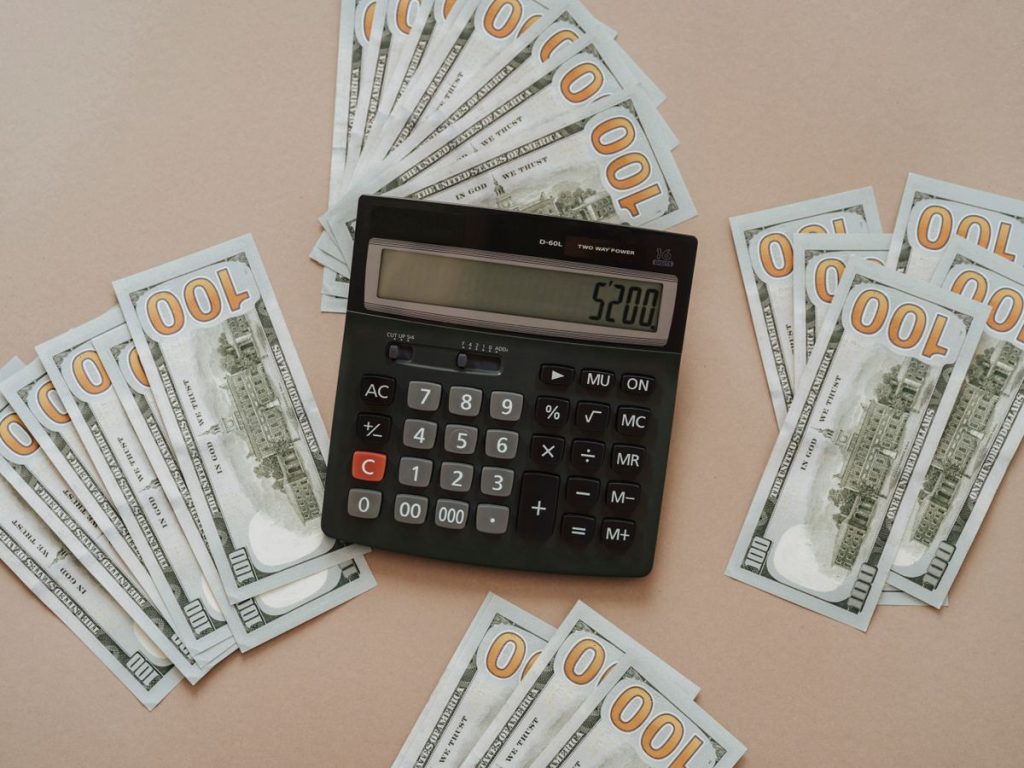 Top view of a calculator showing $5200 surrounded by $100 bills on a tan background