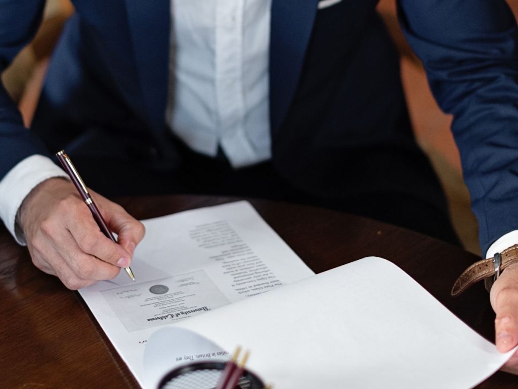 A professional individual signs legal documents at a desk in an office setting