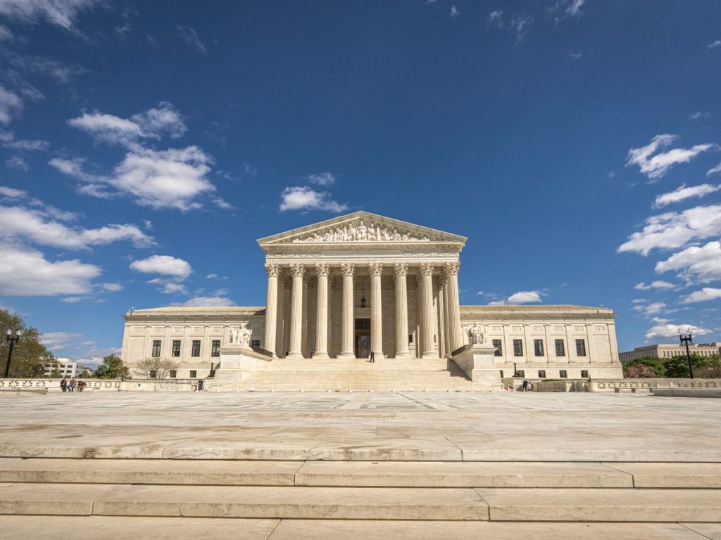 Front view of the United States Supreme Court building on a sunny day with blue sky and clouds
