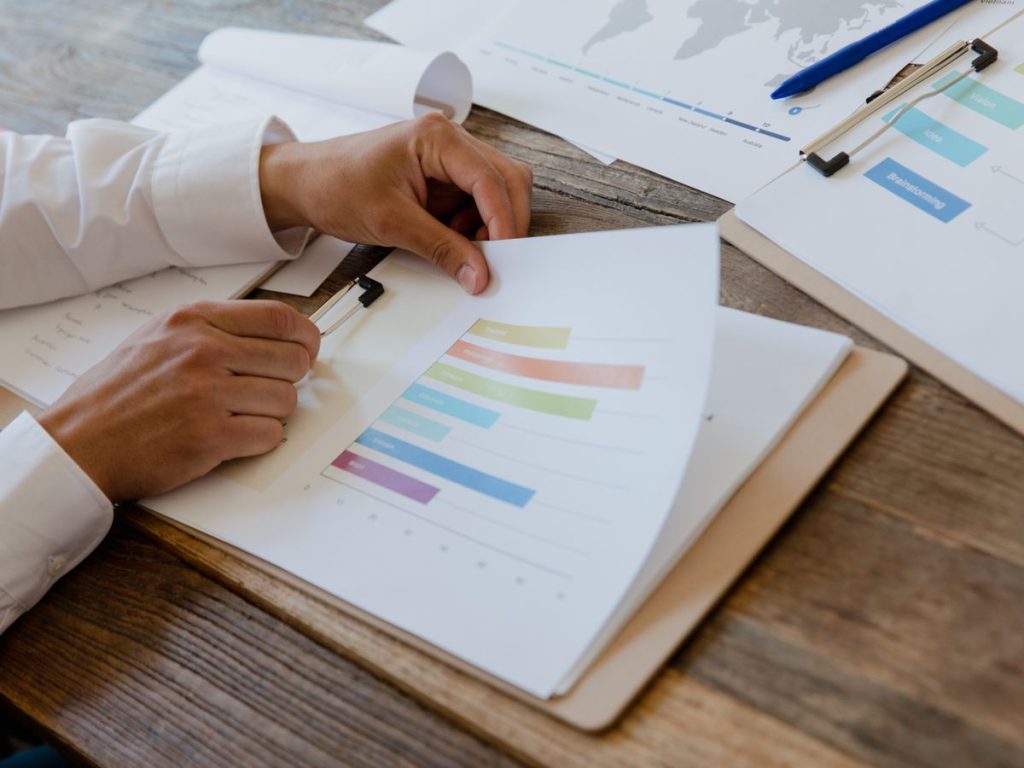 Close-up of hands reviewing business report with colorful charts and graphs on a wooden desk