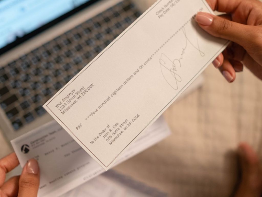 Individual holding a cheque over laptop, signifying online banking or financial transaction