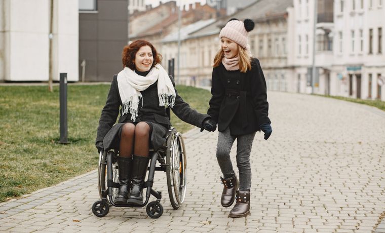 A woman in a wheelchair and a girl share a happy moment outdoors on a cobblestone pathway